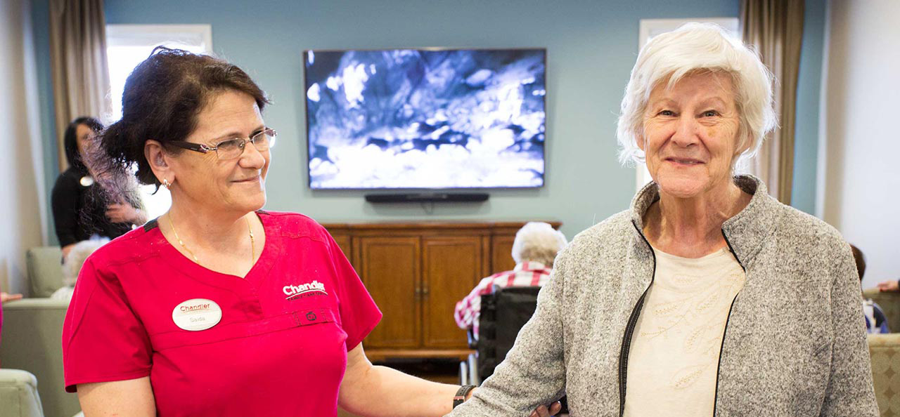 staff member holding hands with senior woman who is smiling at the camera